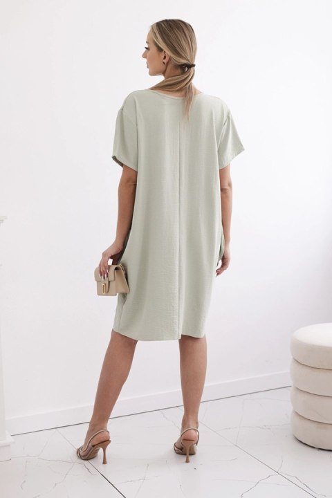 Jasnozielona sukienka z praktycznymi kieszeniami i ozdobnym wisiorkiem